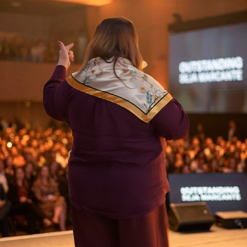 Kátia no palco diante de centenas de mulheres, vista de costas